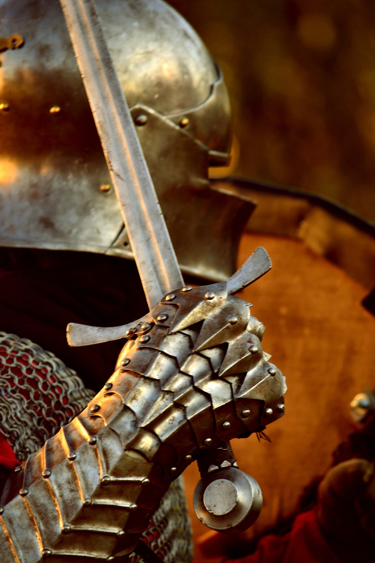A knight in full armour and helmet stands in dusky light, sword and gauntleted fist raised in the foreground, ready for battles